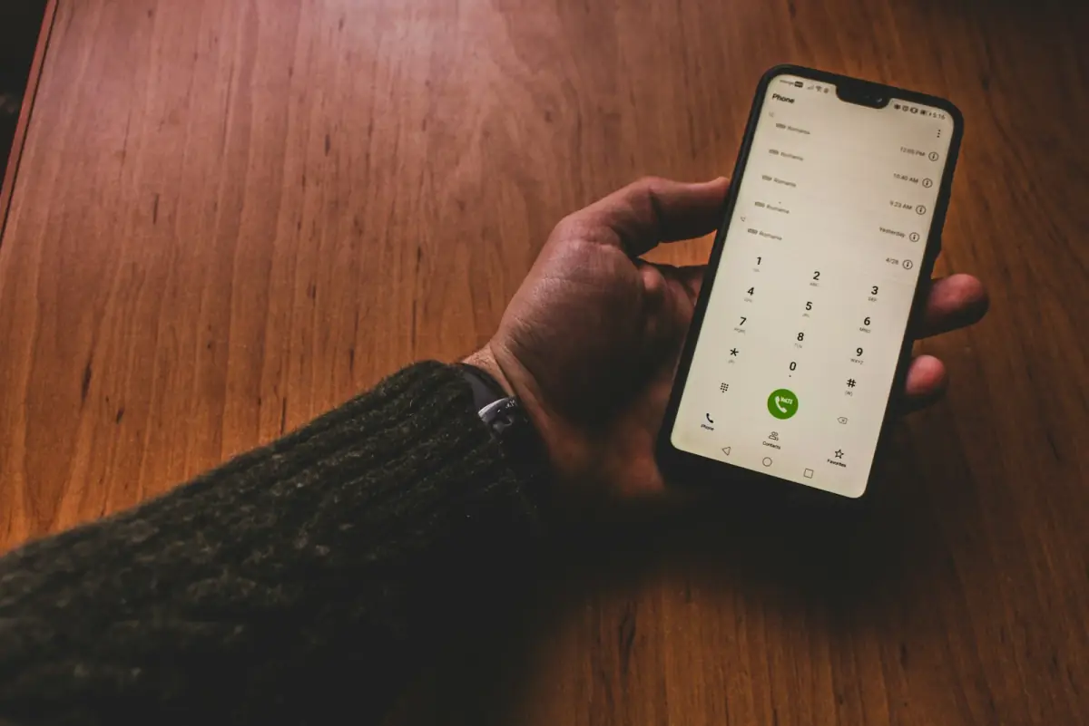 Manos sosteniendo un celular sobre una mesa de madera.