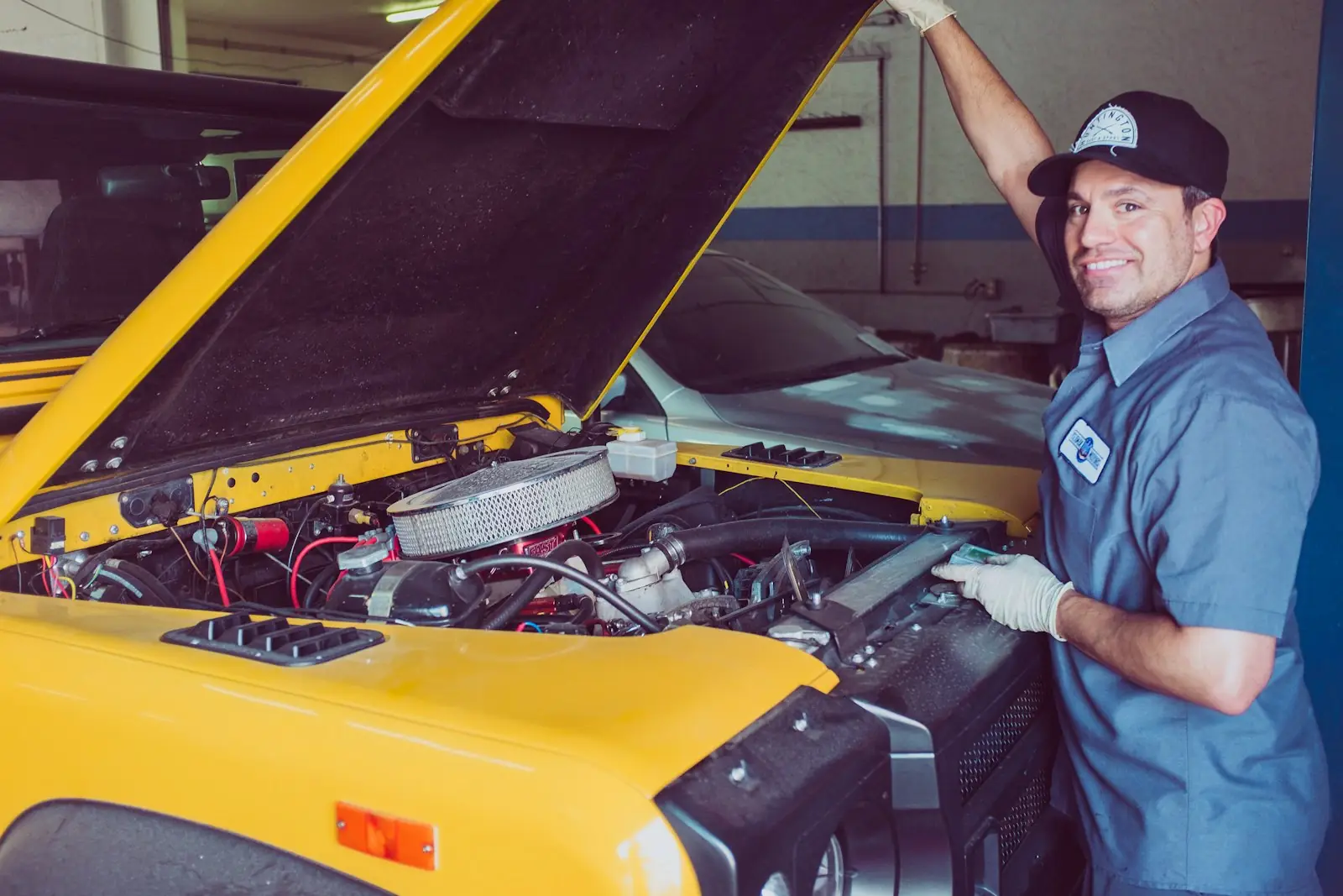 Mecánico sonriendo junto al motor de un carro con el capó abierto.